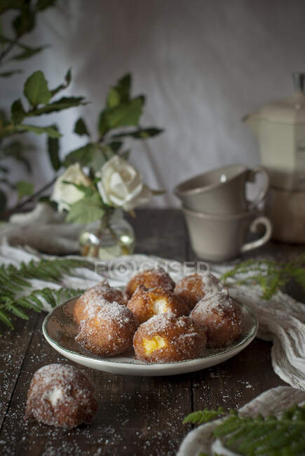 Hausgemachte Puddingcreme-Krapfen mit Zucker bedeckt auf rustikalem Holztisch mit Tischdecke und Blätterdekoration — Stockfoto