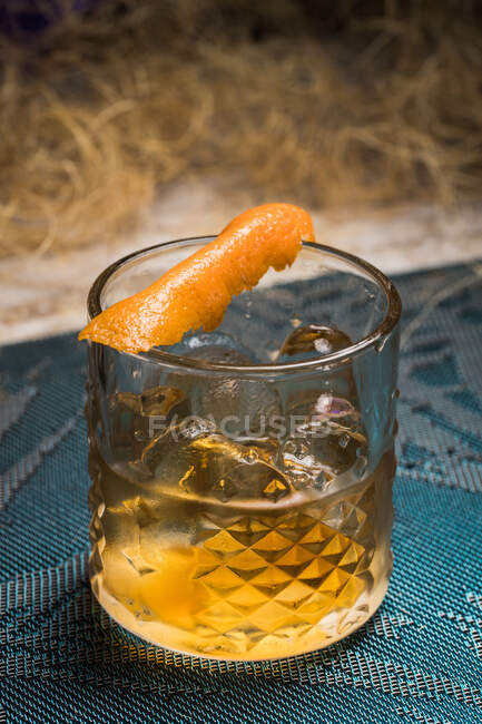 Tazza di vetro Tiki con bevanda vecchio stile collocato su un panno in mezzo all'erba secca contro recinzione in legno e foglie colorate su sfondo sfocato — Foto stock
