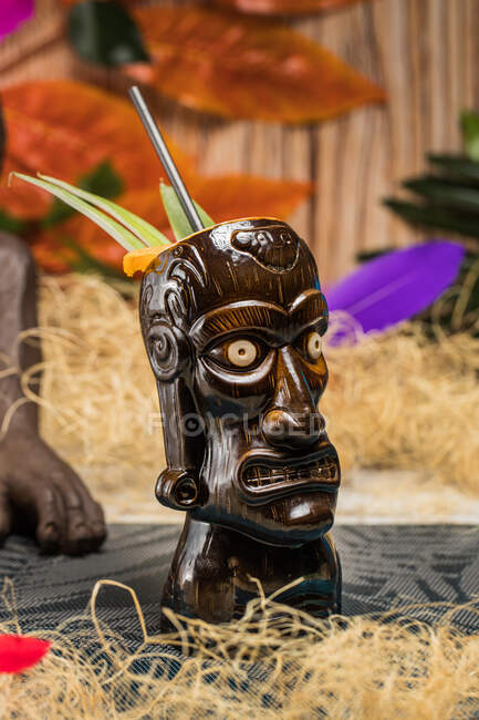 Brown sculptural tiki mug with alcohol drink decorated with straw and ice placed on table — Stock Photo