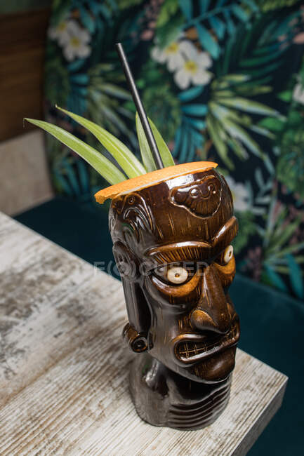 Коричневий скульптурний чашка тікі з алкогольним напоєм, прикрашений соломою і льодом, поміщений на дерев'яний стіл — стокове фото