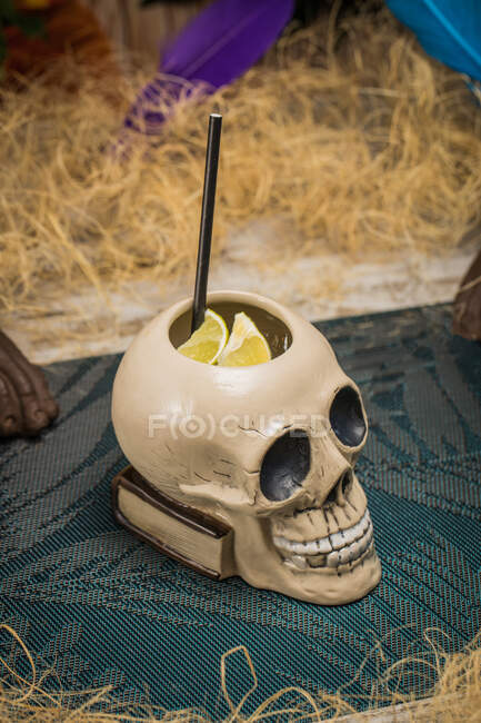 Керамічний полінезійський чашковий череп у формі тікі з соломою, поміщений серед сухої трави з дерев'яним парканом та барвистим пір'ям на розмитому фоні — стокове фото