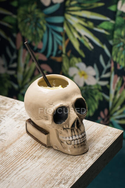 Ceramic polynesian tiki cup skull shaped with straw placed on wooden table on blurred background — Stock Photo
