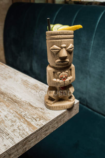 Traditional sculptural tiki cup of alcohol drink with straw placed on wooden table — Stock Photo