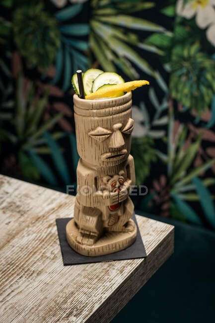 Taza tiki escultórica tradicional de bebida alcohólica con paja colocada en una mesa de madera - foto de stock