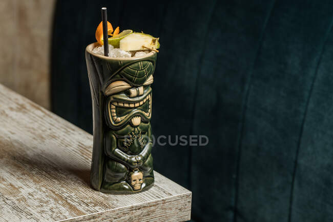 Велика скульптурна чашка, наповнена бузком, прикрашена соломою та фруктами, розміщеними на зеленому килимі на дерев'яному столі — стокове фото
