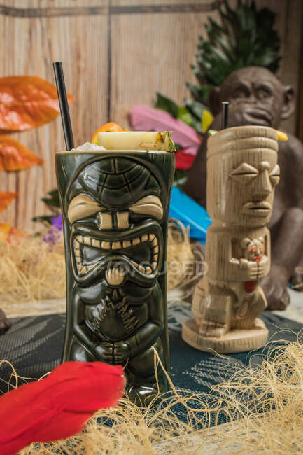 Große skulpturale Tiki-Tasse gefüllt mit Schnaps verziert mit Stroh und Früchten auf grünem Teppich gegen trockenes Gras — Stockfoto