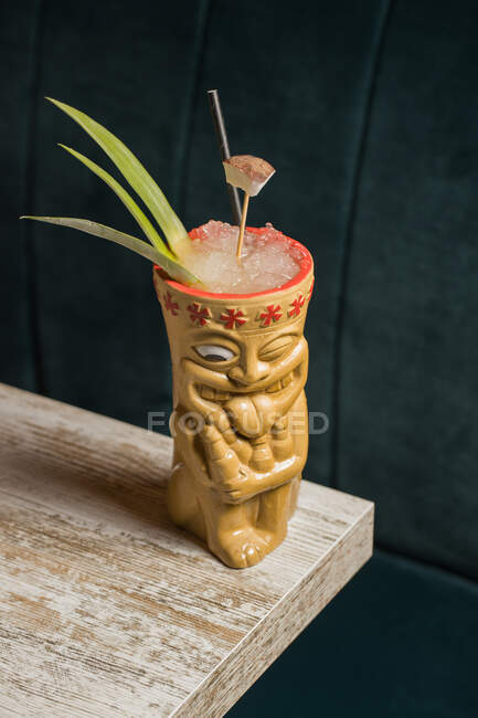 Polynesische Tiki-Tasse mit kaltem Alkohol, dekoriert mit Stroh und grünen Ananasblättern, die auf einem Holztisch stehen — Stockfoto