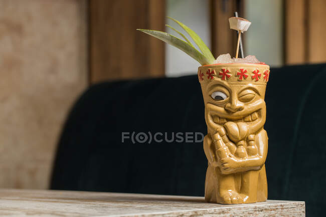 Polynesische Tiki-Tasse mit kaltem Alkohol, dekoriert mit Stroh und grünen Ananasblättern, die auf einem Holztisch stehen — Stockfoto