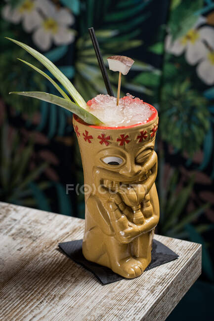 Полінезійська чашка холодного алкогольного напою, прикрашена солом'яним і зеленим листочками ананасів на дерев'яному столі. — стокове фото