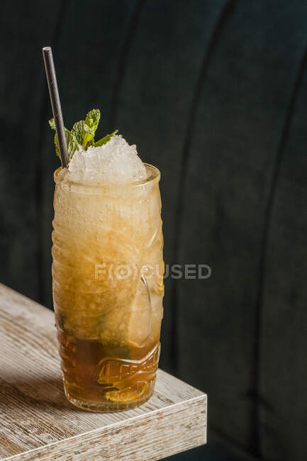 Tasse Tiki avec boisson alcoolisée froide avec de la paille servie avec de la glace et décorée avec de l'herbe fraîche placée sur fond flou — Photo de stock