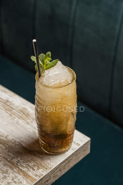 From above of tiki cup with cold alcohol drink with straw served with ice and decorated with fresh herb placed on blurred background — Stock Photo
