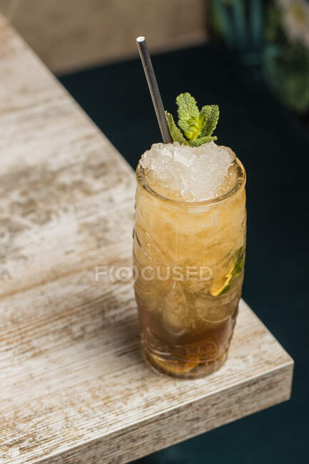 From above of tiki cup with cold alcohol drink with straw served with ice and decorated with fresh herb placed on blurred background — Stock Photo