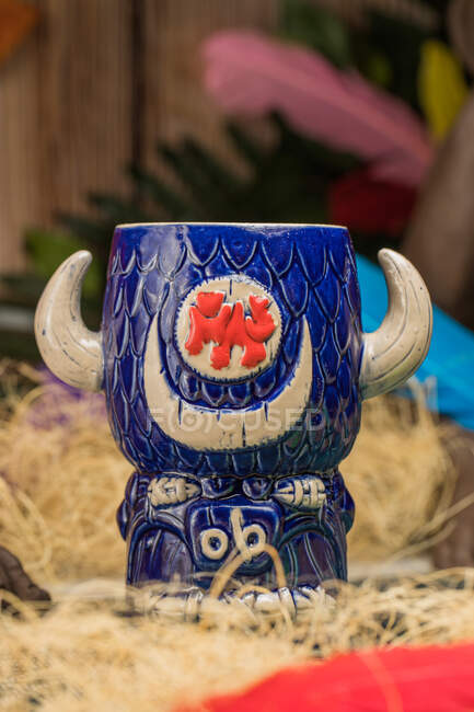 Tasse tiki en forme de taureau de boisson alcoolisée avec mousse placée sur de l'herbe sèche et des plumes sur fond flou — Photo de stock