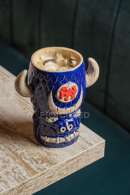 Зверху бика у формі тікі кухоль алкогольного напою з флаконом, розміщеним на дерев'яному столі на розмитому фоні — стокове фото