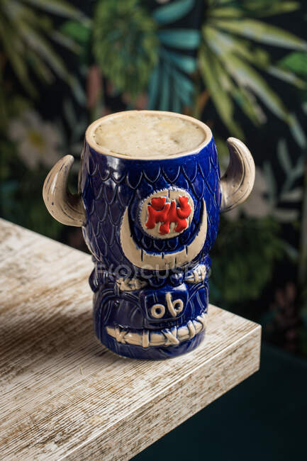 Desde arriba de la taza tiki en forma de toro de bebida alcohólica con espuma colocada contra la mesa de madera sobre fondo borroso - foto de stock