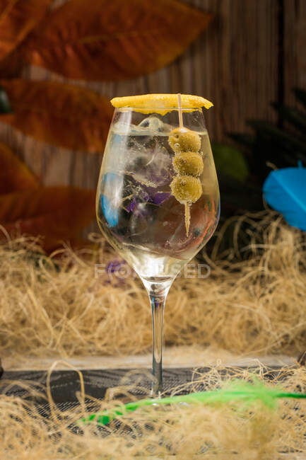 Crystal wineglass with Martini cocktail served with lemon zest and olives edge placed against dry grass — Stock Photo