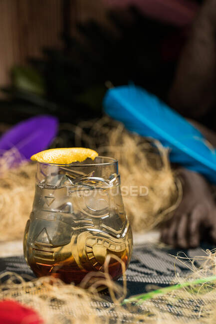 Caneca de vidro Tiki com bebida colocada na borda da mesa de madeira na sala com grama seca no fundo borrado — Fotografia de Stock