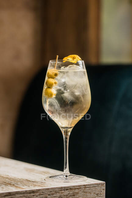 Crystal wineglass with Martini cocktail served with lemon zest and olives edge of wooden table — Stock Photo