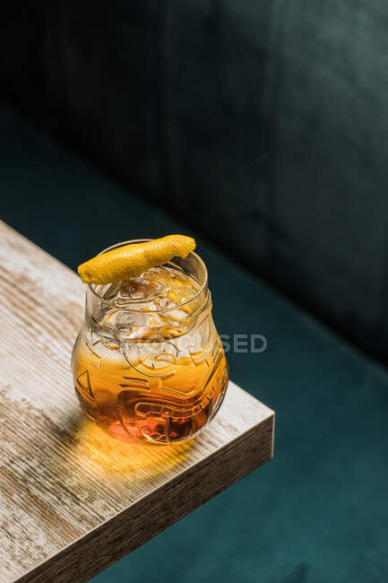 From above of tiki glass mug with booze placed on edge of wooden table in room on blurred background — Stock Photo