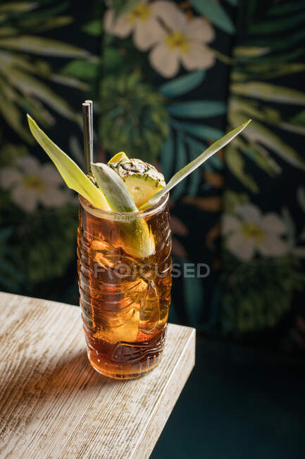 Dall'alto di tazza di tiki di vetro piena di bevanda alcolica con paglia decorata con frutto posto su orlo di divano di tavolo di legno — Foto stock