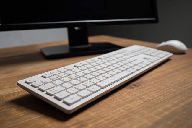 Teclado moderno branco e mouse perto do computador colocado na mesa de madeira — Fotografia de Stock
