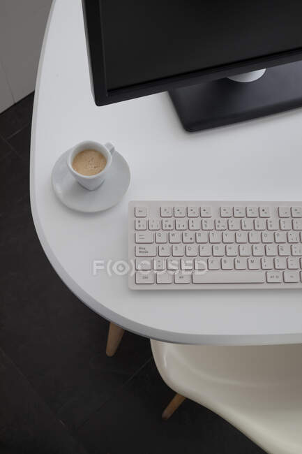 Сверху современный компьютер с черным монитором и белой клавиатурой помещен на стол с кофейной кружкой в офисе — стоковое фото