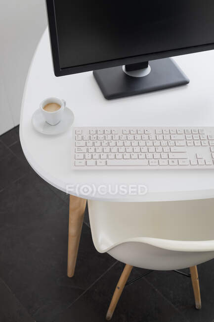 Do computador acima mencionado moderno com monitor preto e teclado branco colocado na mesa com caneca de café no escritório — Fotografia de Stock
