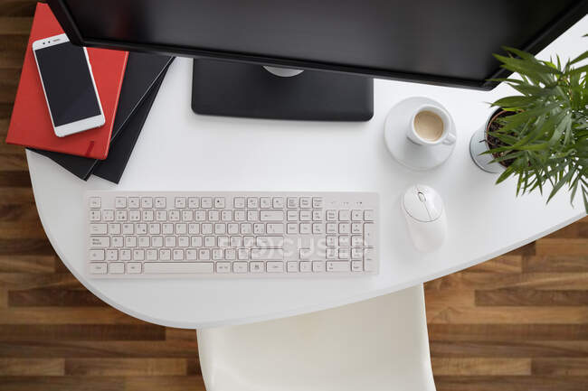 Зверху сучасний комп'ютер і смартфон з блокнотом, розміщеним на білому столі в легкому офісі — стокове фото
