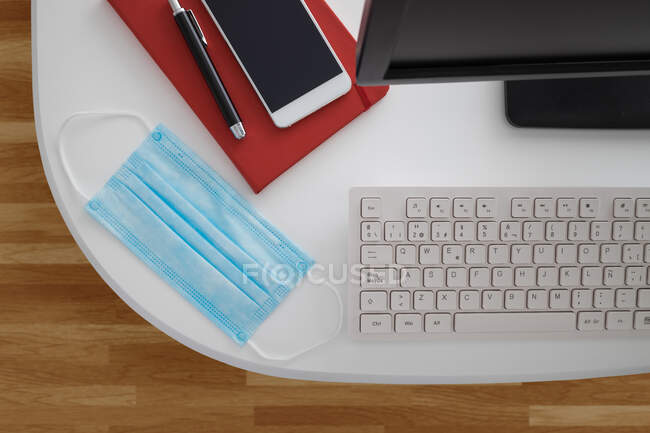 Modern computer and smartphone with notebook placed on white table with medical mask in light office — Stock Photo