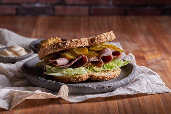 Primer plano de un delicioso sándwich de pastrami, lechuga, jamón y pepinillo - foto de stock