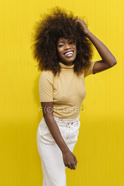 Jeune femme ethnique joyeuse avec coiffure afro touchant les cheveux tout en regardant la caméra au soleil — Photo de stock