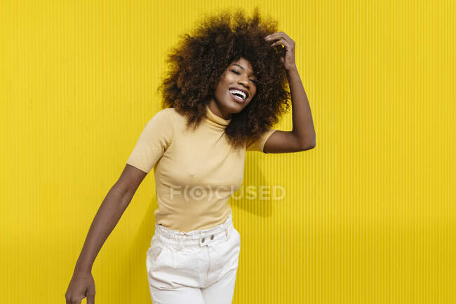 Young cheerful ethnic female with Afro hairstyle touching hair while looking at camera in sunlight — Stock Photo