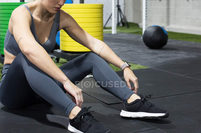 Serious adult sportswoman sitting on floor and resting after intense workout in sport club with various equipment for functional training — Stock Photo