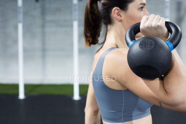 Анонимная спортсменка в спортивной одежде, выполняющая упражнения с тяжелыми гирями во время функциональной тренировки в спортзале — стоковое фото