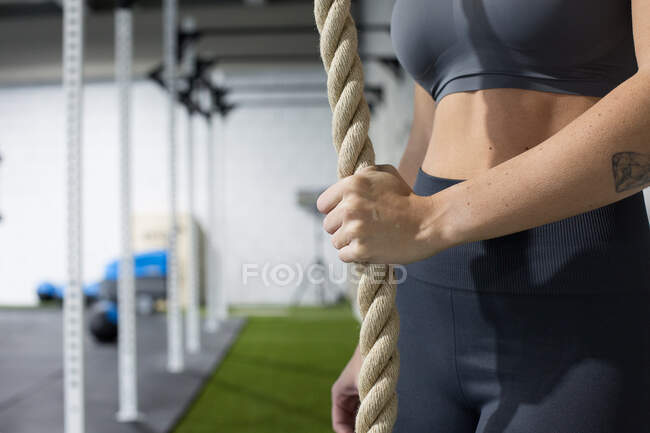 Vista lateral de la hembra de corte anónimo en forma de pie cerca de la cuerda colgante y preparándose para la escalada durante el entrenamiento funcional en el gimnasio - foto de stock