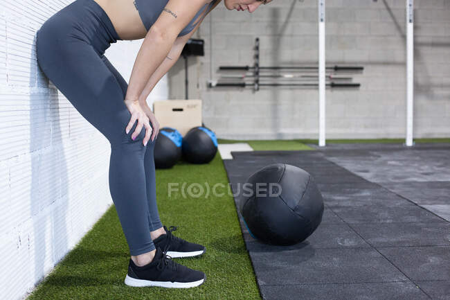 Side view of crop unrecognizable tired sportswoman having break and resting after intense functional workout with medicine ball in gym — Stock Photo
