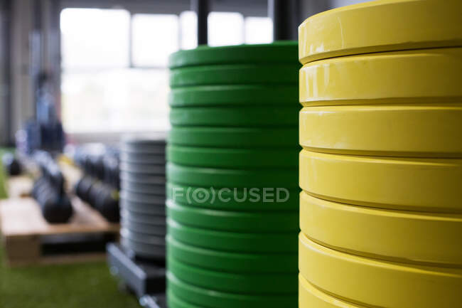 Plaques de poids multicolores en métal lourd empilées sur gazon artificiel dans la salle de gym moderne avec divers équipements sportifs — Photo de stock