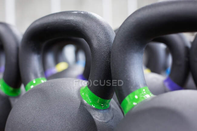 Full frame closeup of heavy black iron kettlebells with colorful weight labels arranged in rows in gym — Stock Photo