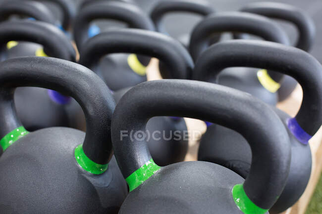 Primer plano de cuadro completo de pesadas pesadas pesas de hierro negro con etiquetas de peso de colores dispuestos en filas en el gimnasio - foto de stock