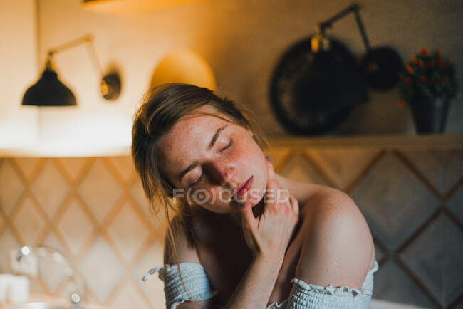 Мрійлива молода жінка з закритими очима ніжно торкається обличчя, стоячи на сучасній кухні — стокове фото