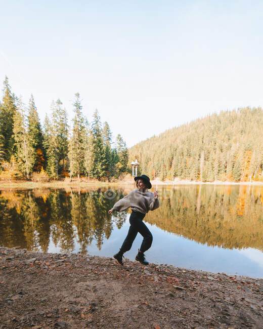 Side view of female tourist running on shore against water reflecting coniferous trees and looking away — Stock Photo