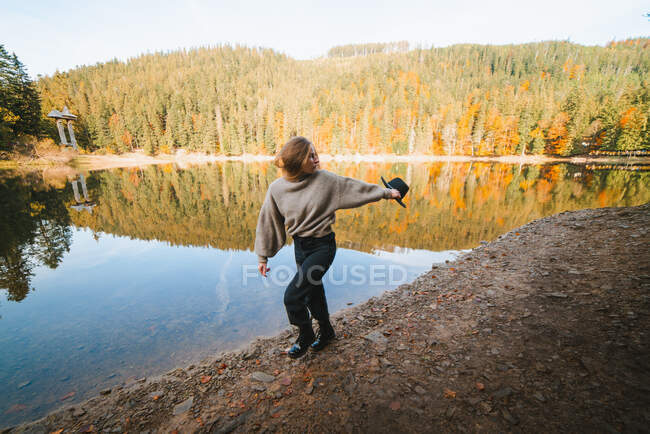 Female tourist walking on shore against water reflecting coniferous trees and looking away — Stock Photo