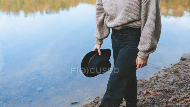 Crop anonymous female traveler in casual wear strolling on coast against transparent water reflecting trees — Stock Photo