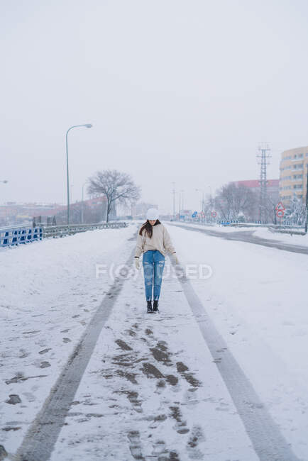 Anonymous female standing on straight roadway with snow and footprints under white sky in Madrid — Stock Photo