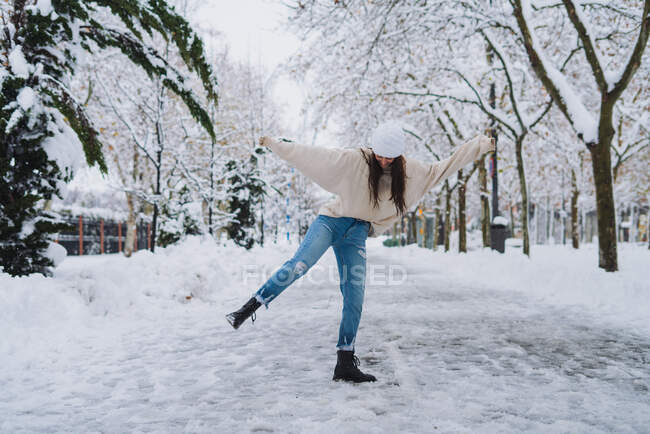 Unrecognizable carefree female standing with raised leg and arms on walkway with footprints in winter city — Stock Photo