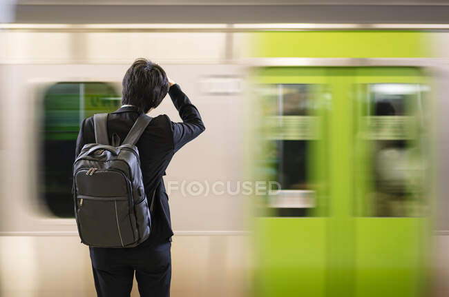 Обратный вид на неузнаваемого бизнесмена-пассажира с рюкзаком, стоящего на платформе станции метро в Токио — стоковое фото