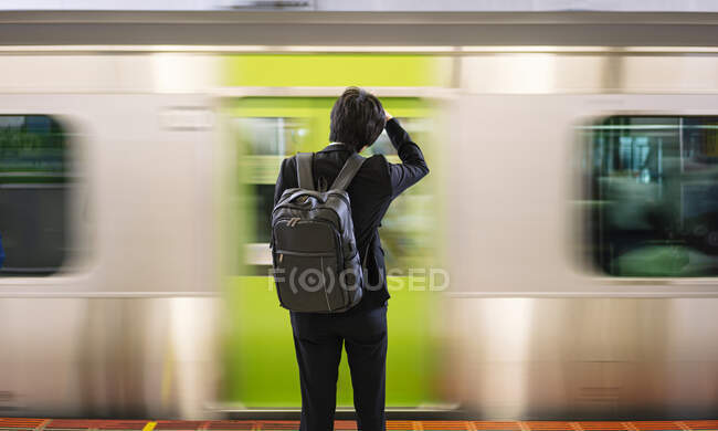 У зворотному вигляді нерозпізнаний пасажир з рюкзаком стоїть на платформі станції метро в Токіо. — стокове фото