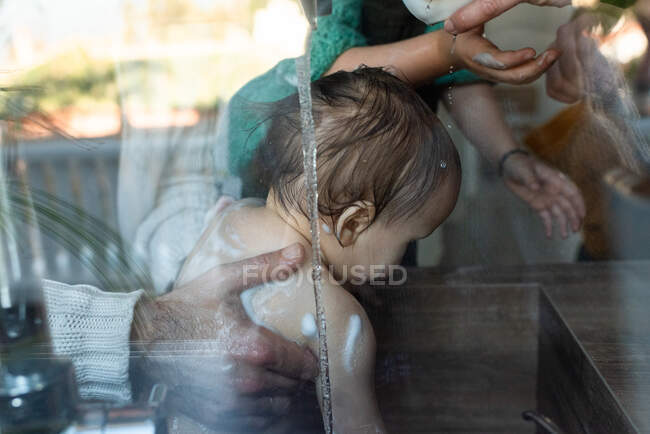 Mãe de cultura irreconhecível e criança banhar adorável criança sentada no lavatório na cozinha em casa — Fotografia de Stock