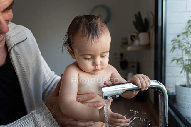 Неупізнаваний батько миє задоволених малюків, які бавляться з крана в раковині. — стокове фото