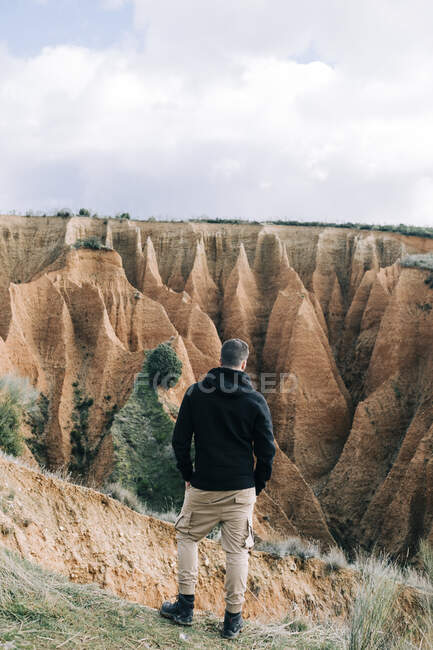 Back view of unrecognizable tourist admiring ravine from mount under cloudy sky in daylight — Stock Photo